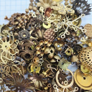May include: A selection of brass-coloured metal embellishments, including floral designs, filigree, and decorative shapes. The assortment features a mix of textures and designs, with a range of sizes and styles, ideal for crafting and jewellery making.