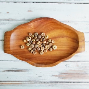 May include: A wooden tray with a natural finish holds a collection of small, dried, light brown and beige flower buds.