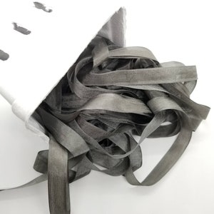 May include: A pile of grey satin ribbon in a white container. The ribbon is soft and silky, and it is perfect for adding a touch of elegance to any project.
