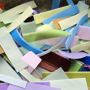 May include: A selection of pastel-coloured velvet ribbons in shades of blue, green, pink, and yellow. The ribbons are cut into short lengths and are scattered, creating a textured and vibrant display. Suitable for craft projects.