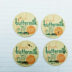 May include: Four round, cream-coloured milk bottle caps with green and orange text. The text reads "Fresh buttermilk, A Healthful Drink, Pasteurized".