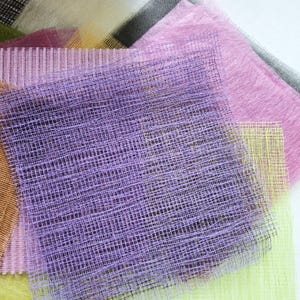 May include: A selection of colourful mesh fabric swatches in shades of purple, pink, green, and grey. The mesh has a grid-like pattern, and some swatches have a fuzzy texture. The fabrics are layered on top of each other.