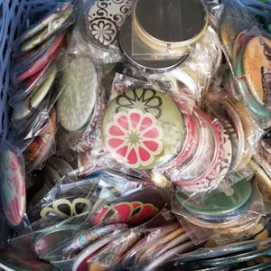 Peut inclure: Une collection de boutons ronds, colorés et à motifs dans différents designs. Les boutons sont emballés dans des sacs en plastique transparent et présentent des motifs floraux, géométriques et abstraits.