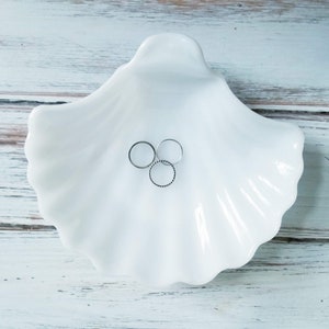 May include: Three silver rings in a white ceramic seashell dish.