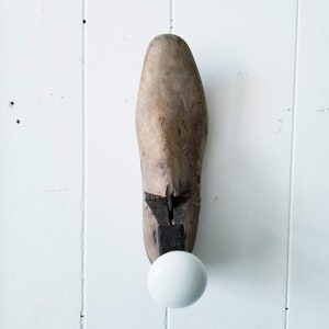 May include: A wooden shoe last with a white ceramic knob. The shoe last is marked with the number "7 1/2 A".