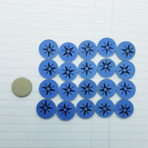 May include: A set of 20 blue and black star-shaped game pieces. The pieces are arranged in a rectangular pattern on a white surface. There is a single round, beige piece in the bottom left corner.