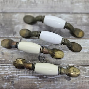 Peut inclure: Quatre boutons de cabinet antiques avec une poignée ovale en céramique blanche et une base en laiton. Les boutons ont une finition vieillie.