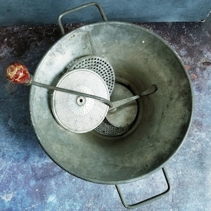 May include: A vintage metal food mill with a red handle and three different sized grates. The mill is made of silver metal and has a handle on each side.