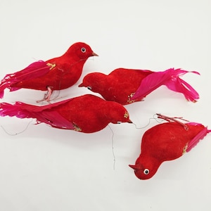 May include: Four red decorative birds with pink feather tails and gold accents. The birds have small beaks and wire legs, set against a white background. These plush birds are likely used for seasonal decor.