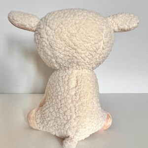 May include: A white plush lamb toy with a fluffy texture. The lamb is sitting with its legs tucked underneath it.