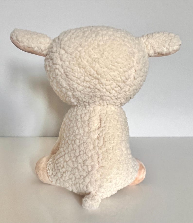 May include: A white plush lamb toy with a fluffy texture. The lamb is sitting with its legs tucked underneath it.