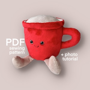 Op de afbeelding: Een rode pluche koffiekop met een lachend gezicht, zwarte knoopogen en beige benen. De beker heeft een witte vulling en een handvat. Tekst op de afbeelding luidt "PDF sewing pattern + photo tutorial."