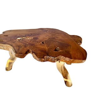 May include: A natural wood coffee table with a unique, irregular shape and a rustic, organic look. The table has a dark brown finish and three legs made from the same wood.