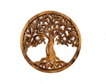 May include: A round, wooden wall hanging featuring a detailed carving of a tree. The tree has a thick trunk, spreading branches, and intricate leaf details. The piece is made of light brown wood and is set within a circular frame.