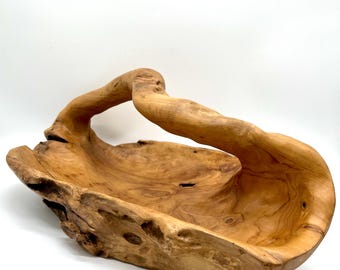 May include: A large, hand-carved wooden bowl with a natural, organic shape. The bowl is made from light brown wood and features a curved handle. The interior of the bowl is smooth, while the exterior has a rough, textured surface. A decorative piece for the home.