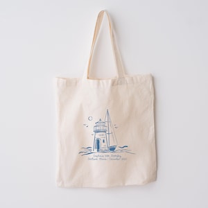 May include: A white canvas tote bag with a blue illustration of a lighthouse and sailboat. The text "August 2020, Sunday, Portland, Maine | December 2023" is printed below the illustration.