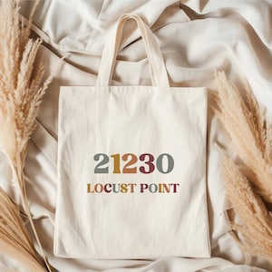 May include: A white canvas tote bag with a colorful design featuring the numbers "21230" and the text "LOCUST POINT".