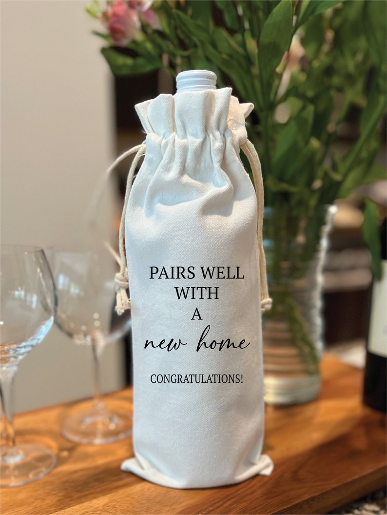 May include: White cotton wine bag with black text that reads "Pairs well with a new home. Congratulations!"