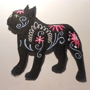 May include: Black embroidered iron-on patch of a French bulldog with floral and swirl designs in pink, blue, and white.