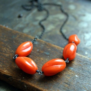 May include: A necklace with a black chain and five bright orange oval-shaped beads.