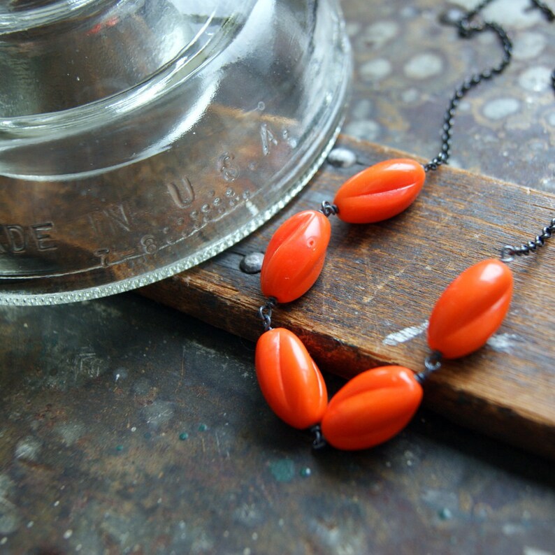 May include: A necklace with a black chain and five orange oval-shaped beads.