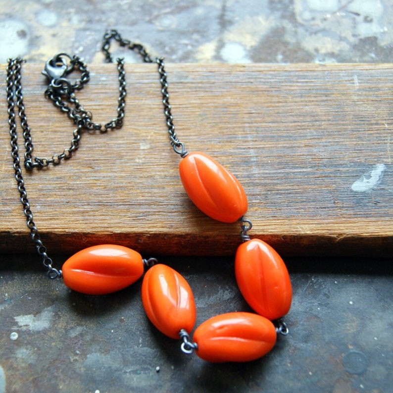 May include: A necklace with a black chain and orange oval-shaped beads. The necklace is lying on a wooden surface.