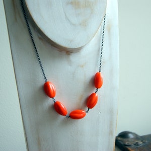 May include: A necklace with a black chain and five bright orange oval-shaped beads.