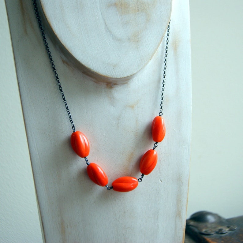 May include: A necklace with a black chain and five bright orange oval-shaped beads.