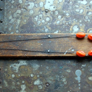 May include: A silver chain necklace with a row of bright orange oval beads.