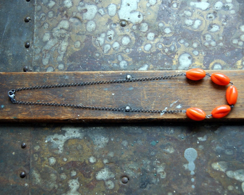 May include: A silver chain necklace with a row of bright orange oval beads.