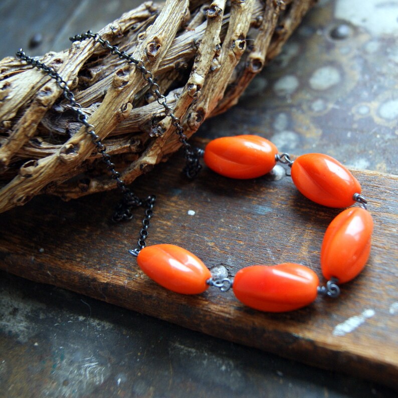 May include: A necklace with a black chain and orange oval-shaped beads. The necklace is lying on a wooden surface.