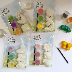 May include: Four "Let's Paint" kits with various plaster figures, including a butterfly, snail, and flower, alongside paint pots and a paintbrush. The kits contain green, purple, orange, and yellow paint. Additional painted butterfly and caterpillar figures are also visible.
