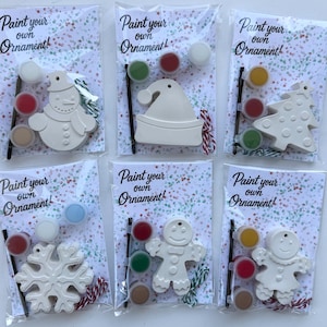 May include: Six individual clear plastic kits labeled Paint your own Ornament! Each kit contains a white ceramic shape, including a snowman, Santa hat, tree, snowflake, and two gingerbread figures, plus three small paint pots and a brush.