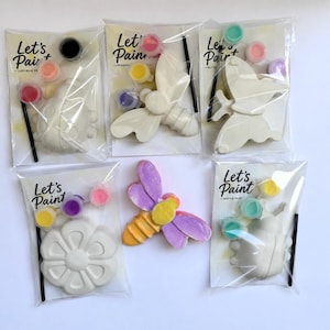 May include: A collection of paint-your-own kits featuring various insect and flower designs. Each kit includes a ceramic figure, paint pots in assorted colors, and a paintbrush. The packaging displays the text "Let's Paint".