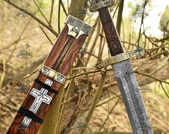 Op de afbeelding: Een zwaard van Damascus-staal met een patroon op het lemmet, een donkerhouten handvat met ingewikkelde knoopmotieven en een koperen pommel. De bijpassende houten schede heeft een zilverkleurige kruisinleg, koperen accenten en zwart koord.
