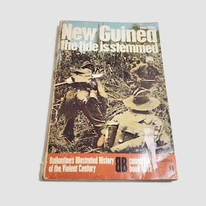 Puede incluir: Una portada de libro de bolsillo vintage con una foto de soldados en un entorno de selva. El título es "Nueva Guinea la marea está contenida" y el libro forma parte de la Historia Ilustrada de Ballantine del Siglo Violento. El número del libro es 13.