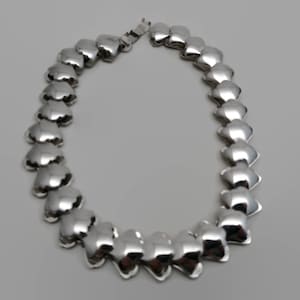 May include: A silver necklace with a chain made of linked heart-shaped charms.