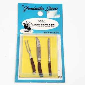 May include: A pack of doll accessories, labelled "Grandmother Stover's Doll Accessories Made in U.S.A. Ohio". The pack contains a silver fork, knife, and a silver utensil with a brown handle.