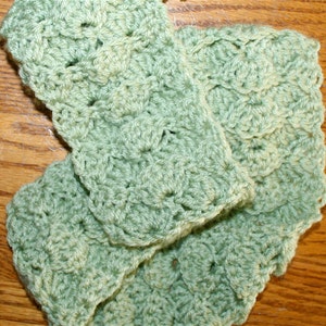 May include: A green crocheted scarf with a textured pattern. The scarf is made of soft yarn and has a delicate, feminine look.