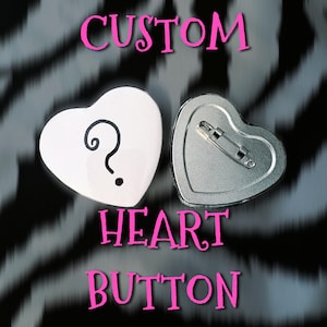 May include: Two heart-shaped buttons, one white with a black question mark and one silver metal with a pin backing. The text CUSTOM HEART BUTTON is displayed in pink letters. The buttons are arranged to show both the front and back sides clearly.
