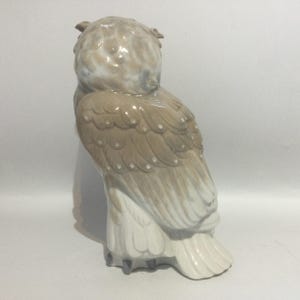 May include: A ceramic owl figurine in shades of beige, brown, and white. The owl is depicted in a seated position, with detailed feather patterns and a textured surface. The figurine has a classic, decorative style.
