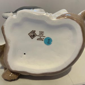 May include: A ceramic figurine of a seated animal, possibly a rabbit or dog, with a white belly and brown and gray accents. The figurine has a glossy finish and a blue sticker with the number 515.