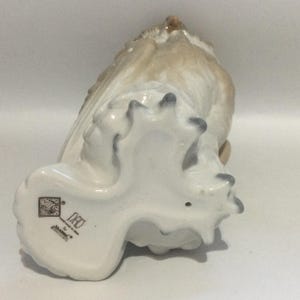 May include: A ceramic owl figurine in shades of white, beige, and gray. The owl is perched, with its wings partially spread. The underside of the figurine shows the owl's feet and a maker's mark. The figurine is a decorative item.