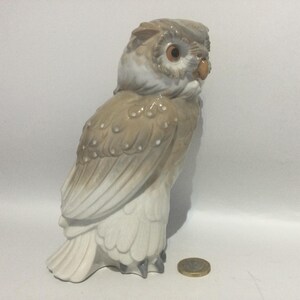 May include: A ceramic owl figurine in shades of beige, brown, and white. The owl has detailed feather textures, large eyes, and a small beak. The figurine is standing upright, showcasing its detailed design.