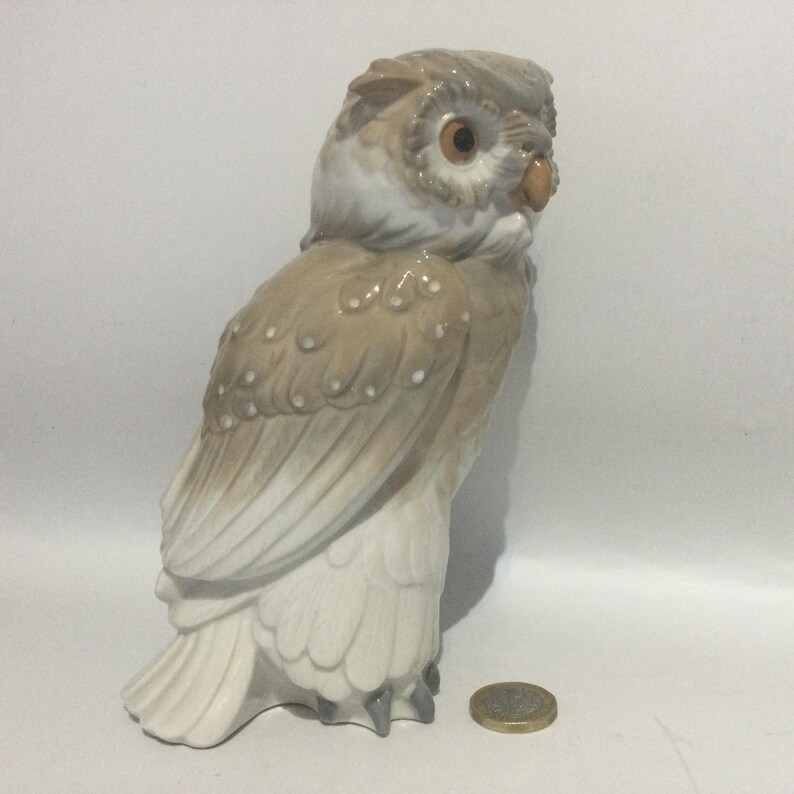 May include: A ceramic owl figurine in shades of beige, brown, and white. The owl has detailed feather textures, large eyes, and a small beak. The figurine is standing upright, showcasing its detailed design.