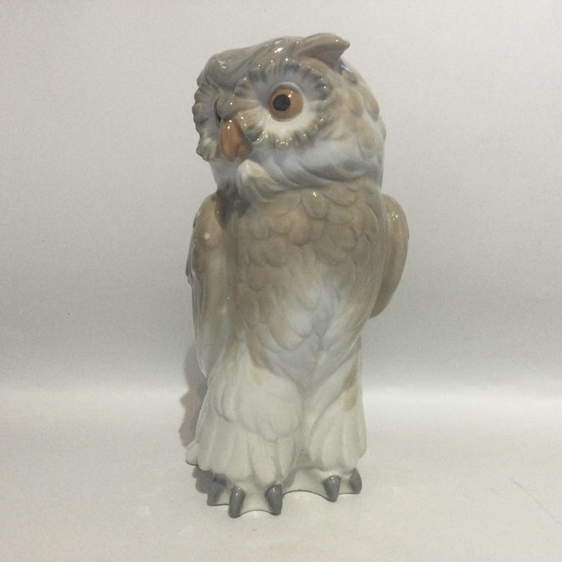 May include: A ceramic owl figurine in shades of gray, brown, and white. The owl has large, round eyes and detailed feather textures. The figurine is standing upright, showcasing its detailed features.