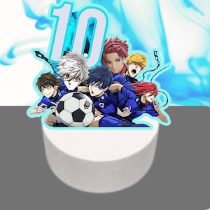 May include: Cake topper featuring a soccer ball and a group of anime characters in blue uniforms. A large number 10 in light blue is at the top. The background has a blue and white design.