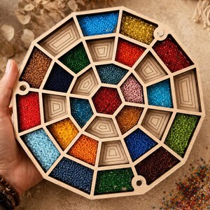 May include: A circular wooden organizer tray featuring multiple geometric compartments filled with small, colorful glass beads in shades of red, blue, green, yellow, and orange. The tray has a light wood finish and a radial, segmented design.