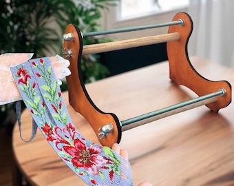 May include: A wooden beading loom with two metal rods and a gray beaded necklace with red and green floral designs.