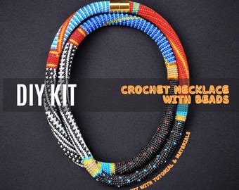 May include: DIY kit for a crochet necklace with beads. The kit includes a black and white beaded necklace, a red, blue, and yellow beaded necklace, and a tutorial.  The text "DIY KIT" and "CROCHET NECKLACE WITH BEADS" is visible in the image.  The text "FULL KIT WITH TUTORIAL & MATERIALS" is also visible in the image.